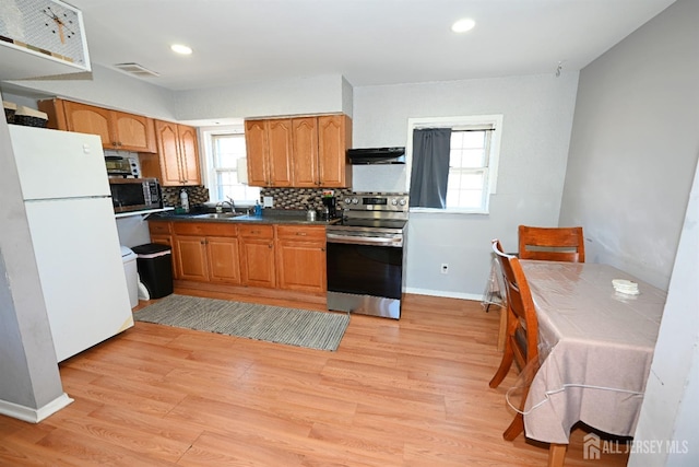 kitchen featuring stainless steel appliances, under cabinet range hood, backsplash, light wood-style floors, and dark countertops