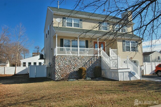view of front of home with a front lawn, a chimney, covered porch, and fence