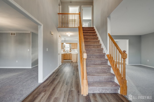 staircase featuring visible vents, wood finished floors, carpet, baseboards, and a towering ceiling