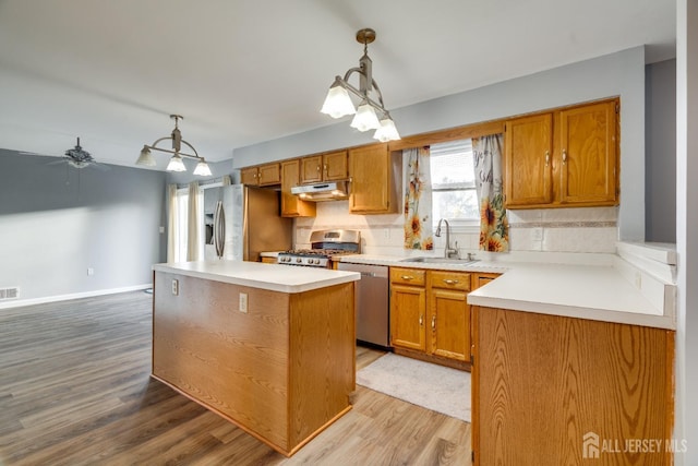 kitchen with brown cabinets, under cabinet range hood, a sink, a center island, and appliances with stainless steel finishes