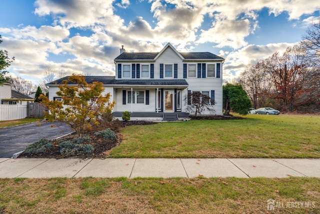 colonial-style house with aphalt driveway, a chimney, a front yard, and fence