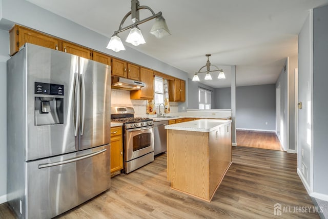 kitchen with under cabinet range hood, stainless steel appliances, light wood finished floors, and light countertops