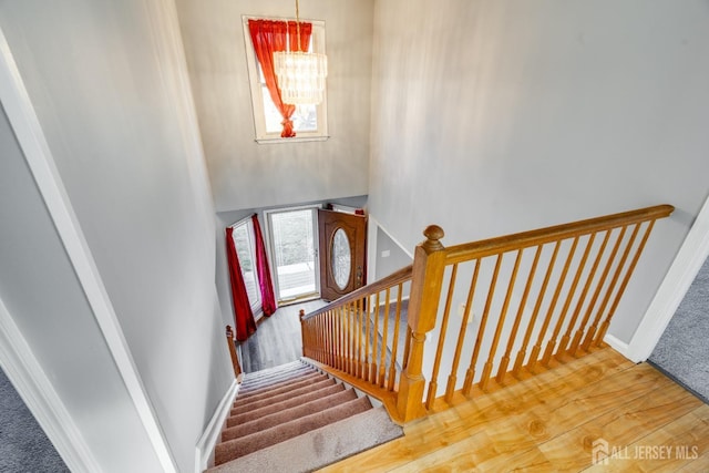 staircase featuring wood finished floors, baseboards, and a chandelier