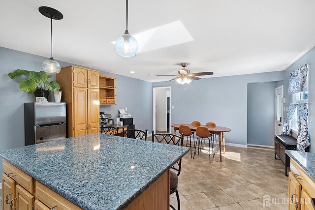 kitchen featuring freestanding refrigerator, a kitchen island, dark stone counters, a ceiling fan, and a skylight