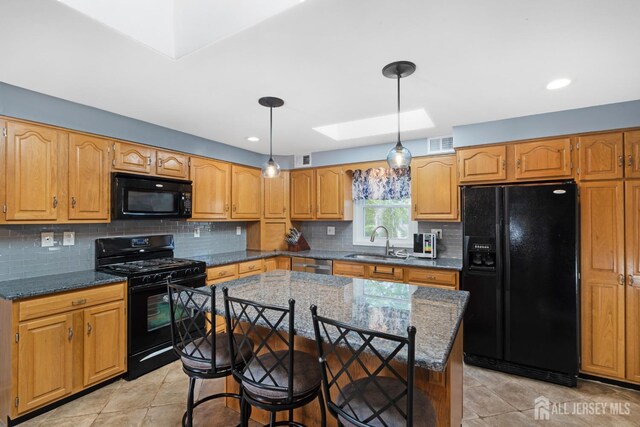 kitchen with visible vents, a sink, dark stone countertops, black appliances, and a skylight