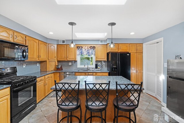 kitchen featuring decorative backsplash, visible vents, a sink, black appliances, and a breakfast bar