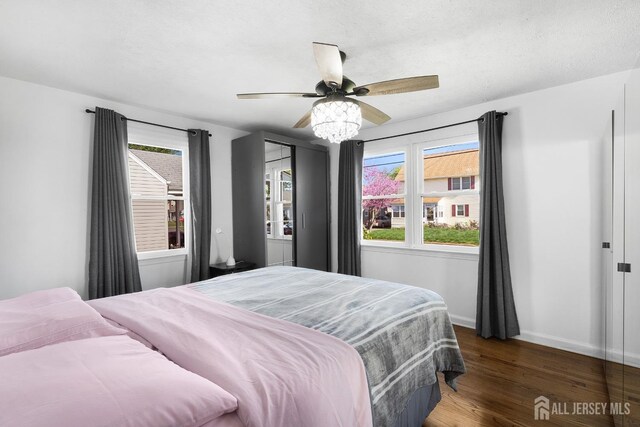 bedroom featuring baseboards, a ceiling fan, wood finished floors, and multiple windows