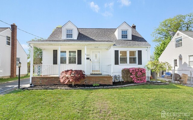cape cod-style house featuring fence, a shingled roof, a front lawn, a porch, and a chimney