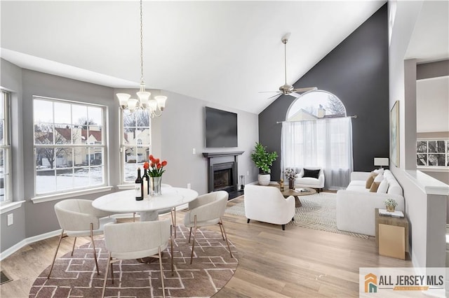 dining area featuring ceiling fan with notable chandelier, wood-type flooring, and high vaulted ceiling