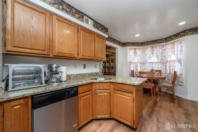 kitchen with a peninsula, light wood-style flooring, a sink, light stone counters, and dishwasher