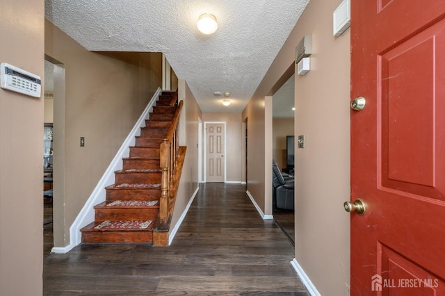 foyer entrance with stairway, a textured ceiling, baseboards, and dark wood-style flooring