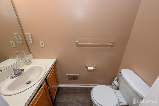 half bath with wood finished floors, visible vents, toilet, vanity, and baseboards