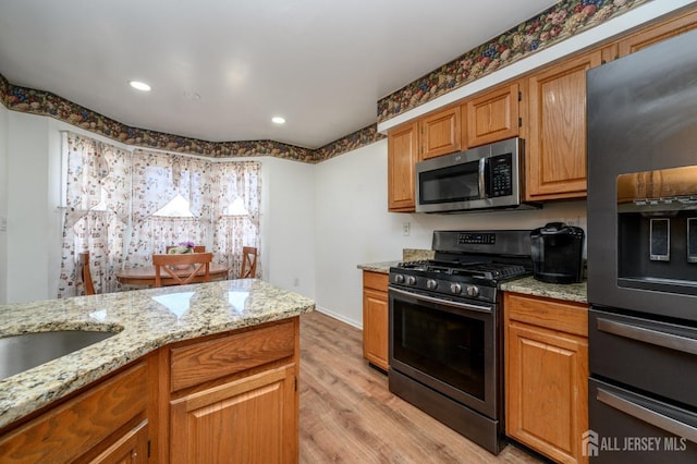kitchen with light wood-style floors, appliances with stainless steel finishes, and light stone counters