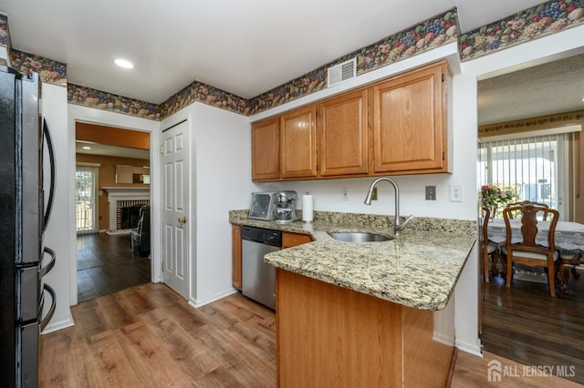 kitchen featuring stainless steel appliances, a peninsula, a sink, a healthy amount of sunlight, and wood finished floors