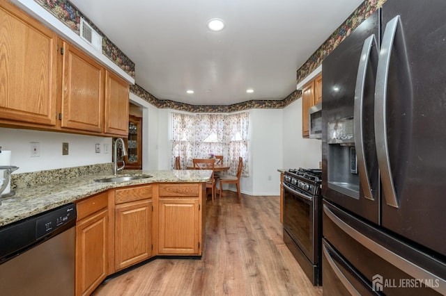 kitchen featuring light wood finished floors, stainless steel appliances, a peninsula, a sink, and light stone counters