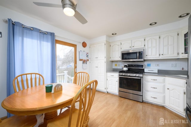 kitchen with backsplash, white cabinets, appliances with stainless steel finishes, and light wood-type flooring