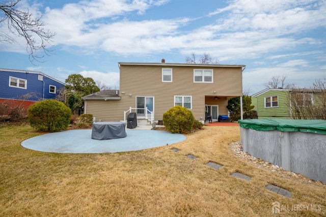 rear view of property featuring a covered pool, a lawn, and a patio