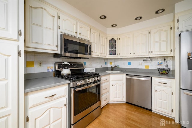 kitchen with a sink, stainless steel appliances, light wood-type flooring, and backsplash