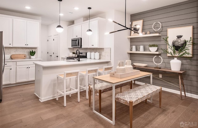 kitchen with light wood-type flooring, stainless steel appliances, decorative light fixtures, an inviting chandelier, and white cabinets