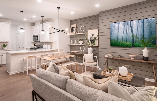 living room with an inviting chandelier, sink, light hardwood / wood-style floors, and wood walls