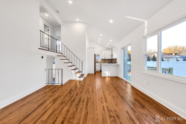 unfurnished living room featuring vaulted ceiling, stairway, baseboards, and wood finished floors