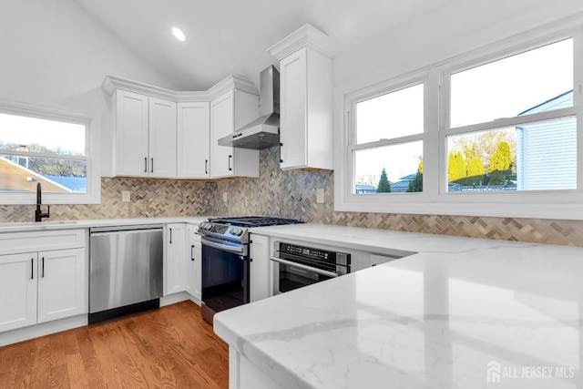 kitchen with tasteful backsplash, lofted ceiling, appliances with stainless steel finishes, wall chimney range hood, and a sink