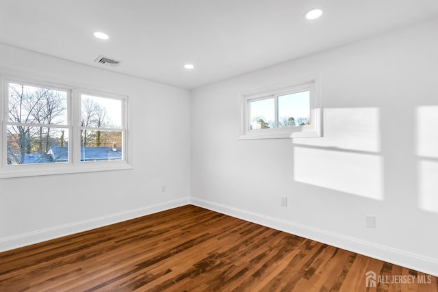 unfurnished room featuring plenty of natural light, wood finished floors, visible vents, and baseboards