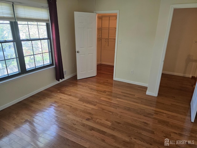 unfurnished bedroom with baseboards, a spacious closet, wood finished floors, and a closet