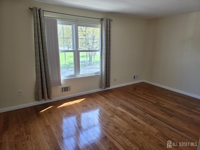 spare room featuring baseboards, plenty of natural light, wood finished floors, and visible vents