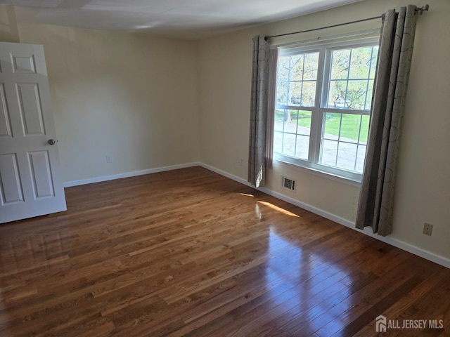spare room featuring baseboards, a wealth of natural light, dark wood finished floors, and visible vents