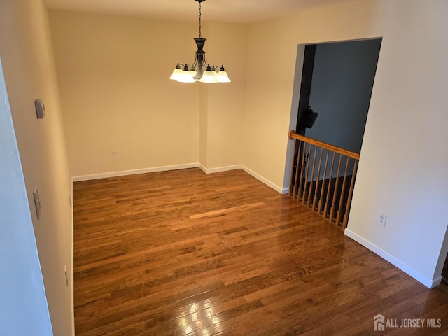 empty room with baseboards, wood finished floors, and a notable chandelier