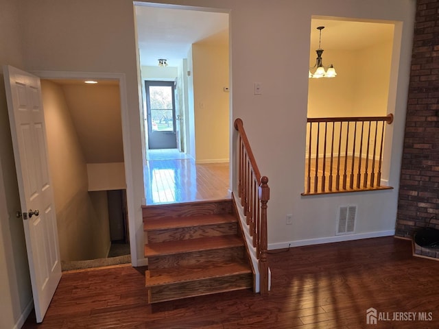 staircase with visible vents, wood finished floors, and an inviting chandelier