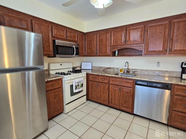 kitchen featuring appliances with stainless steel finishes, light stone counters, a sink, a ceiling fan, and light tile patterned floors