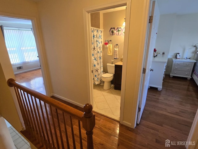corridor featuring baseboards, visible vents, wood finished floors, and an upstairs landing