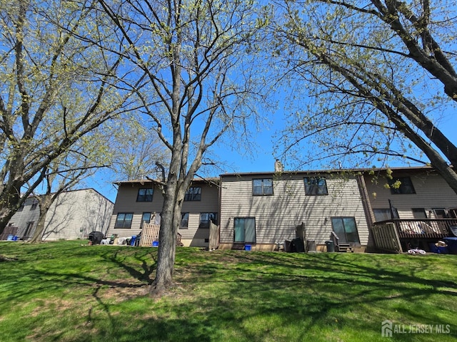 rear view of property with a lawn, a wooden deck, and a chimney