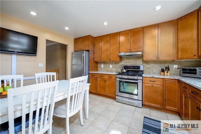 kitchen with brown cabinets, under cabinet range hood, backsplash, appliances with stainless steel finishes, and a toaster