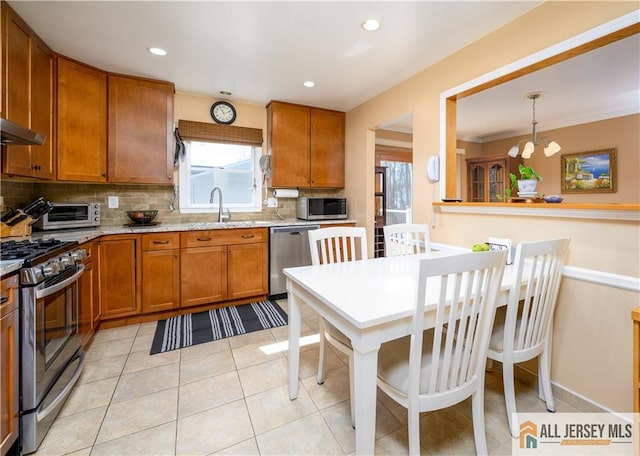 kitchen featuring light tile patterned flooring, a sink, decorative backsplash, appliances with stainless steel finishes, and brown cabinets