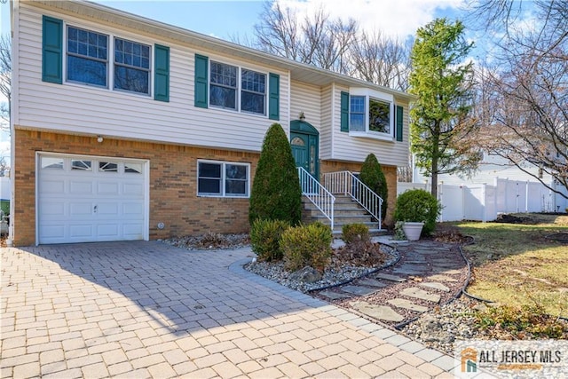 bi-level home featuring brick siding, an attached garage, decorative driveway, and fence