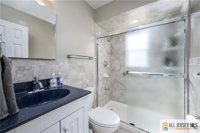 bathroom with toilet, tile walls, a stall shower, and vanity