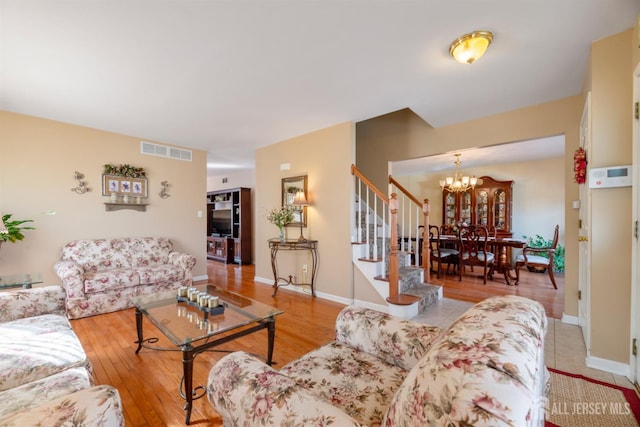 living area with stairway, baseboards, visible vents, light wood-type flooring, and a chandelier