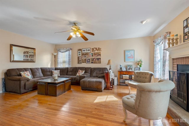 living room with light wood finished floors, a healthy amount of sunlight, a fireplace, and a ceiling fan