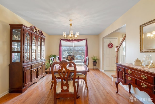 dining area with light wood-style floors, baseboards, a notable chandelier, and stairway