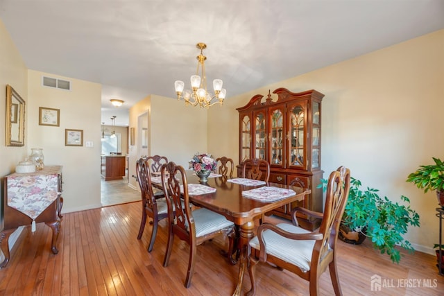 dining room with visible vents, light wood-style flooring, baseboards, and an inviting chandelier