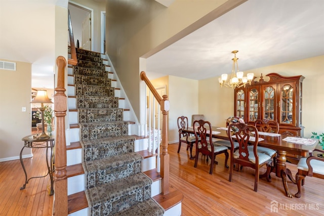 staircase featuring a notable chandelier, visible vents, baseboards, and wood-type flooring