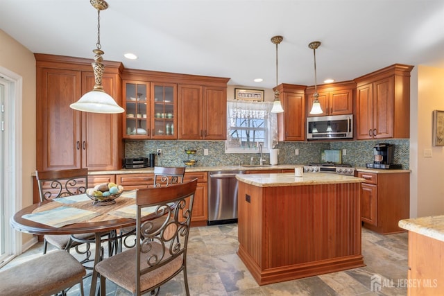 kitchen with decorative backsplash, a sink, stainless steel appliances, brown cabinetry, and glass insert cabinets