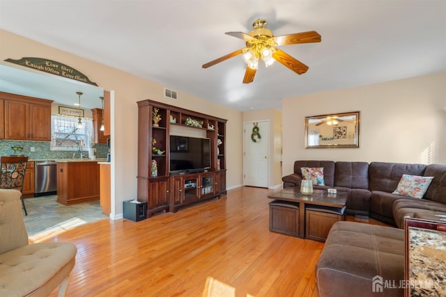 living room featuring a ceiling fan, visible vents, light wood finished floors, and baseboards