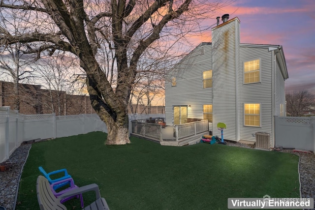 back of property with central air condition unit, a deck, a fenced backyard, a yard, and a chimney