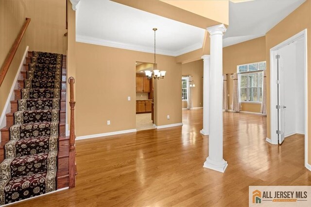 interior space featuring a notable chandelier, crown molding, decorative columns, and light wood-type flooring