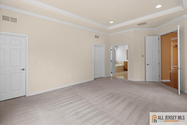 unfurnished bedroom with crown molding, light colored carpet, a raised ceiling, and ensuite bath