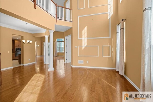 interior space with ornate columns, ornamental molding, a notable chandelier, a towering ceiling, and hardwood / wood-style floors